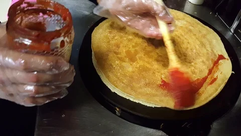 Cook putting some tomato sauce on crepe on a black cooker Stock Footage 103881532