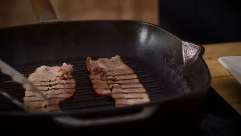 A cook putting two pieces of fried bacon from broiler pan on a white plate. 4K Stock Footage 82358369