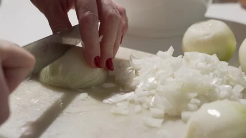 A cook with red nails slices a white onion on a cutting board with a sharp knife Stock Footage 322748482