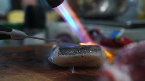 A cook in a restaurant kitchen uses a gas burner to fry cod, fish Stock Footage 140990255