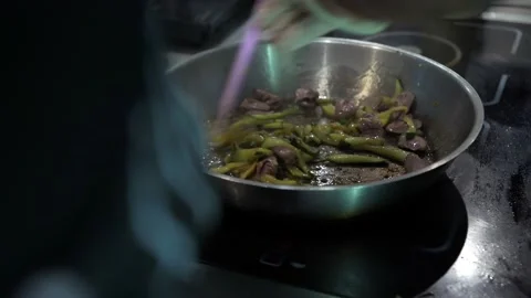 A cook in a restaurant kitchen uses a spatula to stir a dish in a frying pan. Video stock 141414420