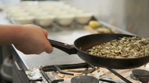 The cook roasts pumpkin seeds in a pan Stock Footage 220572027