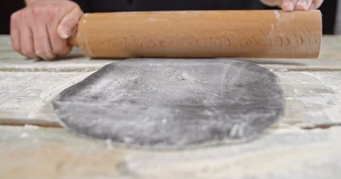 Cook with a rolling pin roll out the black dough pizza Stock Footage 113424340
