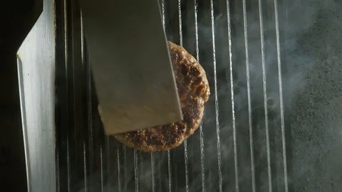 Cook with a silver spatula flips the patty, which is grilled Stock Footage
