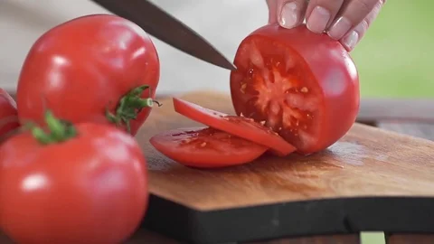 The cook slices tomato by sharp knife on the wooden board outdoors, making of Stock Footage 77576092