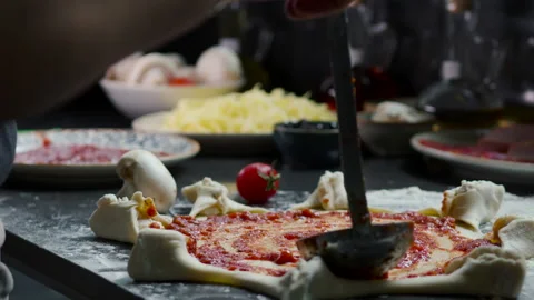 Cook spreading tomato sauce on rolled out pizza Stock Footage 229780166