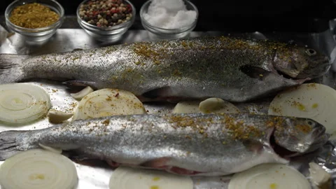 Cook sprinkles salt on two prepared trout fish carcasses on baking sheet Stock Footage 305329658