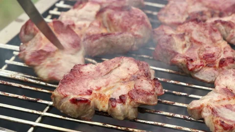 A cook stabs chunks of meat on a barbecue grill with a knife close up Stock Footage 136022129