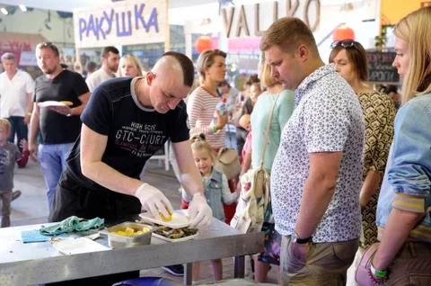 Cook standing at the kitchen table and opening cockle-shell of oyster with a Foto stock