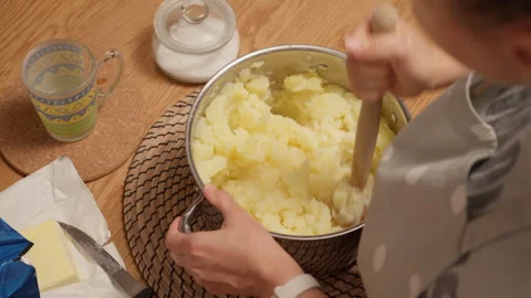 A cook stirs mashed potatoes in a pot on a table with salt and butter Stock Footage 315404361