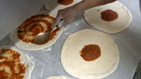 The cook on the table smears tomato paste on a pizza circle in circular motions Stock Footage 104866106
