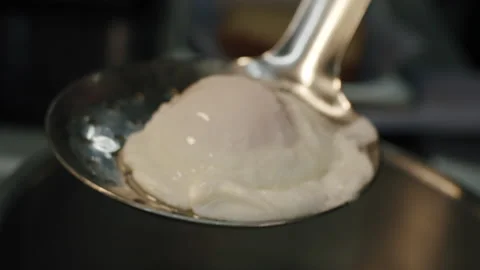 Cook takes out a poached egg with a slotted spoon from boiling water with dumps Video stock 150762836