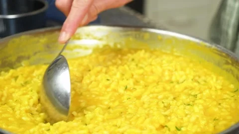 The cook takes the pumpkin risotto from the pan with a spoon. Stockbeeldmateriaal 207018526