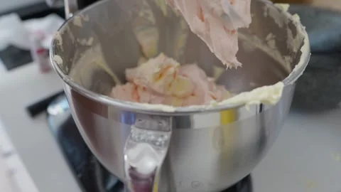 A cook taps a spatula on the side of a mixer bowl then turns it on low to whip Stock Footage 319514790