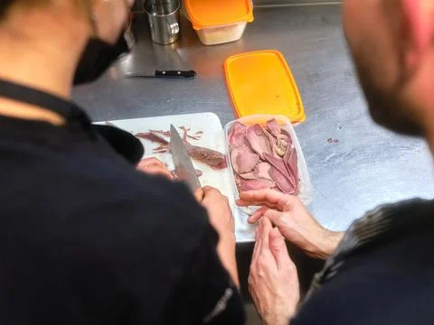 Cook teaching a kitchen assistant how to chop meat in a kitchen Stock Photos
