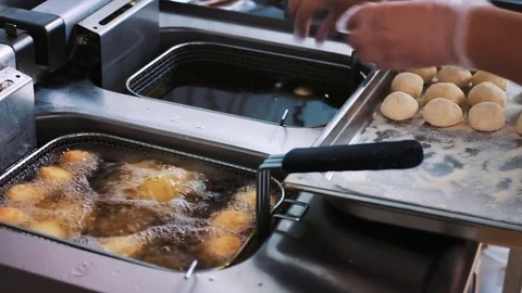 The cook throws the dough into the deep fryer with hot oil. Cooking. Donuts Stock Footage 77453168