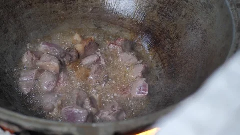The cook throws pieces of meat into a hot iron pot. mixes the meat Stock Footage 125523850