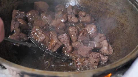 The cook throws pieces of meat into a hot iron pot. mixes the meat (liver) Stock Footage 125696142