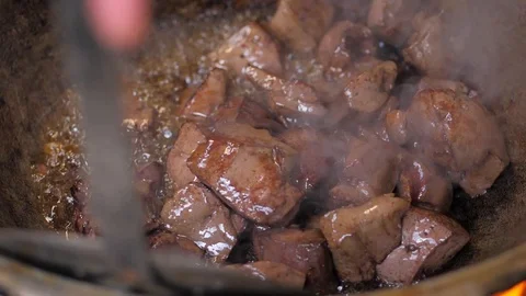 The cook throws pieces of meat into a hot iron pot. mixes the meat (liver) Stock Footage 125745842