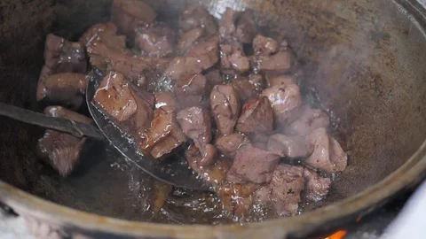 The cook throws pieces of meat into a hot iron pot. mixes the meat (liver) Stock Footage 125745936