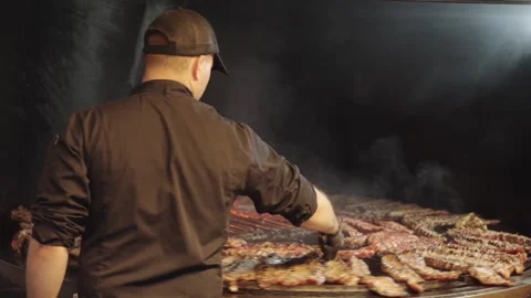 Cook Turning Pork Ribs While Grilling Them on a Rotisserie Video stock 345521899