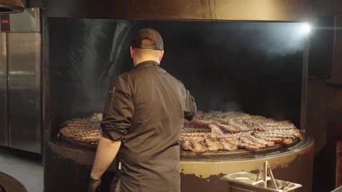 Cook Turning Pork Ribs While Grilling Them on a Rotisserie Video stock 345521901