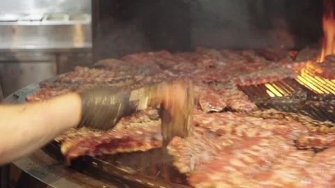 Cook Turning Pork Ribs While Grilling Them on a Rotisserie Video stock 345521902