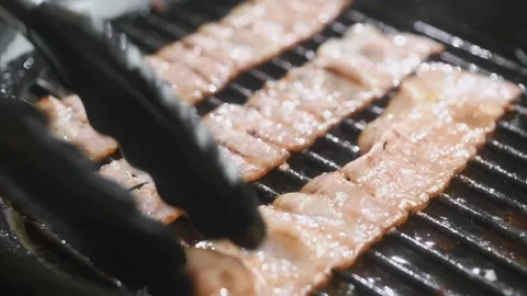 The cook turns the bacon in a grill pan. Stock Footage 198533749