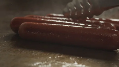 Cook turns forceps fried sausages on an electric stove. Cooking hot dogs Stock Footage 117295953