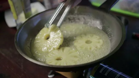 Cook turns pineapples in a pan Stock Footage 96995813