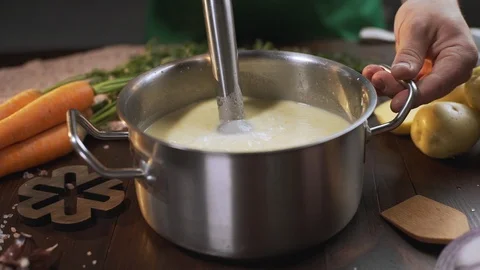 The cook uses hand blender to make mashed soup in the metal pan, cooking healthy Stock Footage 115258551