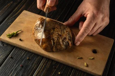 A cook uses a sharp knife to cut a piece of cooked meat on a wooden cutting.. Stock Photos