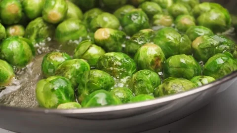 A cook uses a spatula to stir roasting brussel sprouts in a shiny frying pan and Stock Footage 301920616