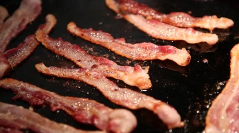 A cook using a spatula to move bacon around on a hot griddle. Stock Footage 60756393
