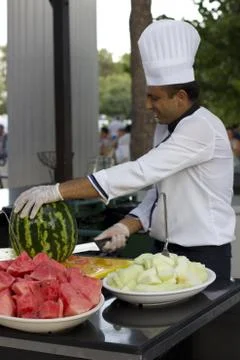 Cook in a white cap cuts a big watermelon Stock Photos