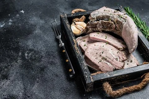 Cooked Boiled veal or beef tongue sliced in a wooden tray. Black background. Top Stock Photos