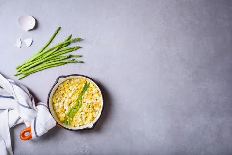 Cooked breakfast, pan of fried scrambled eggs with asparagus on grey table Stock Photos