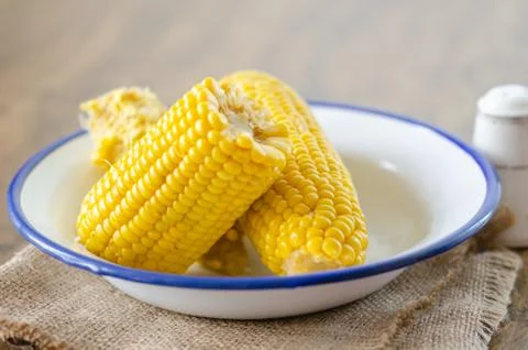 Cooked corncobs in white dish on rustic napkin. Stock Photos