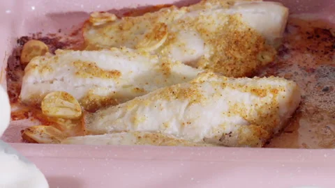 Cooked fish fillets in a pink baking dish with golden garlic seasoning. Stock Footage 308230252