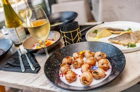 Cooked grape snails in shells on a table in a restaurant with a glass of wine Stock Photos