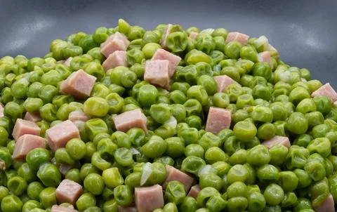 Cooked green peas with diced ham served in a dark grey bowl Stock-Fotos