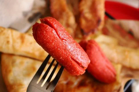 Cooked hot dogs on a fork close to other food items Stock Photos