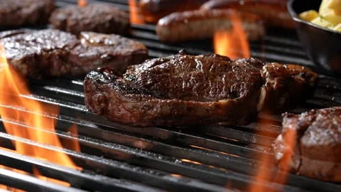 Cooked juicy steak meat beef on a flaming grill surrounded by other meat Stock Footage 170318199