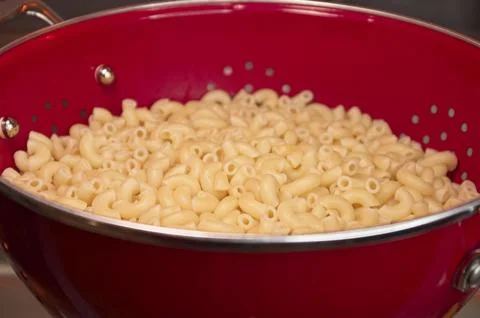 Cooked macaroni cooling in a red colander Stock Photos