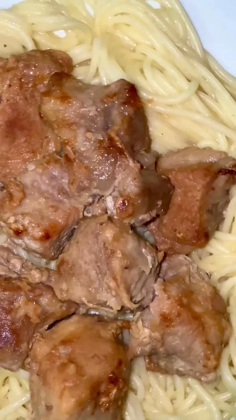 Cooked meat chunks served over spaghetti on white plate Stockbeeldmateriaal 334593518