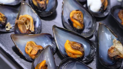 Cooked mussels in open shells slowly rotating on a dark slate serving tray Видео 347181909