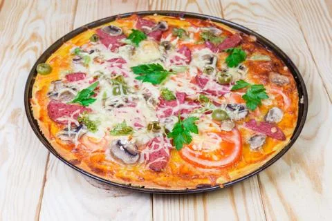 Cooked pizza with salami close-up on rustic wooden table Фото