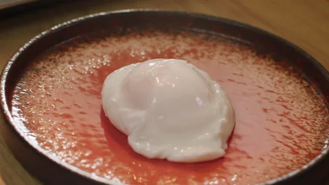 The cooked poached egg is laid out  on a fiery red stylish plate in slow motion 스톡 동영상 150762861
