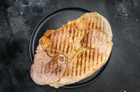 Cooked pork shoulder with bone grilled and seasoned presented on dark plate.. Stockfoto's