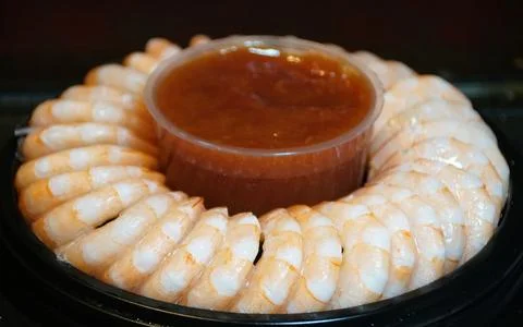 Cooked shrimp arranged in a circular pattern around chilled cocktail sauce .. Stock Photos